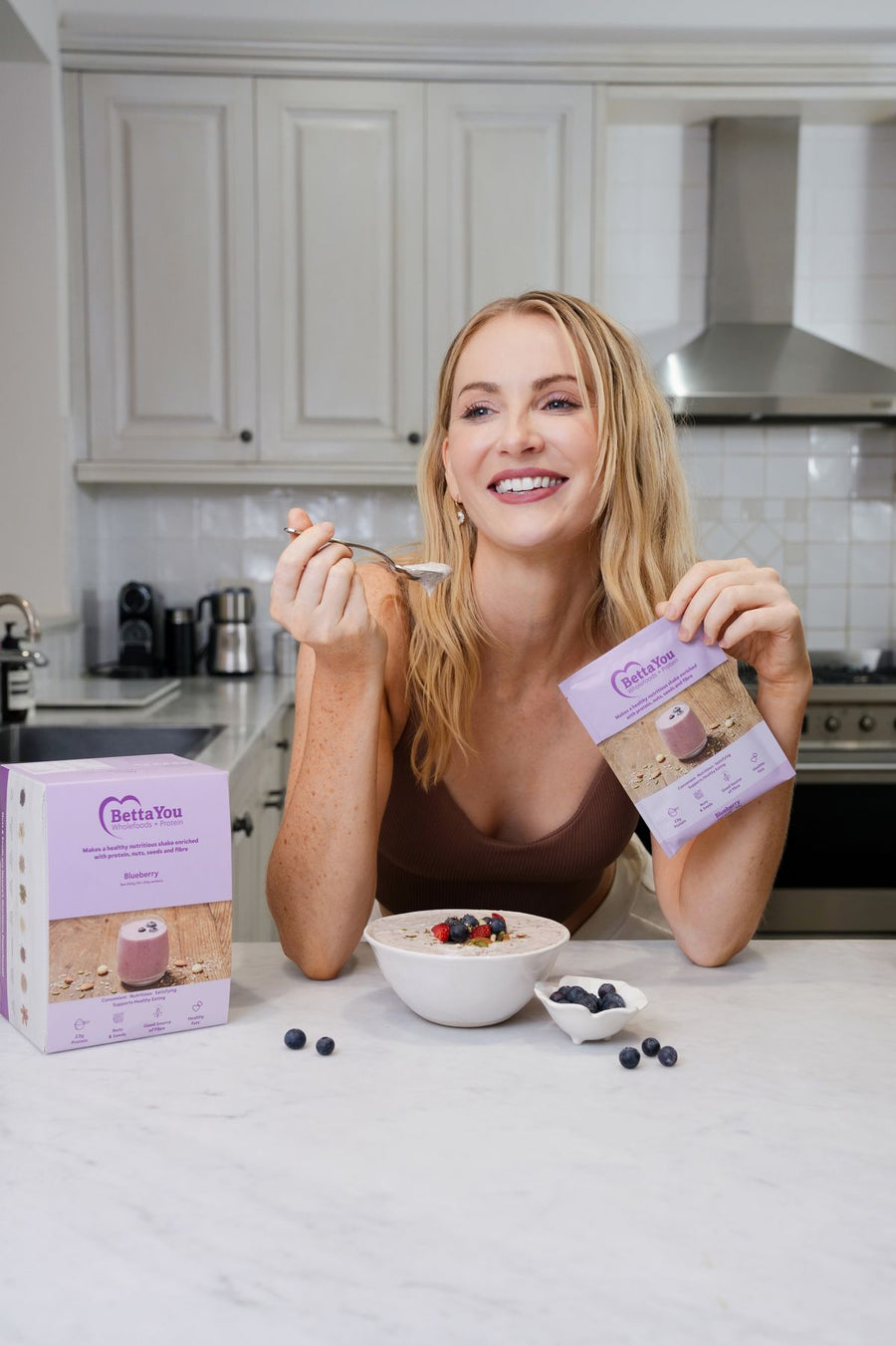 Smiling woman enjoying a high protein BettaYou breakfast bowl at her kitchen bench